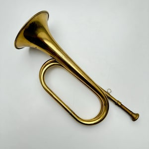 May include: A vintage brass bugle with a bell-shaped mouthpiece and a long, curved tube. The bugle has a gold finish and is in good condition.