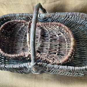 Può includere: Un set di due cesti rettangolari impilabili realizzati con rami di salice intrecciati color marrone scuro e grigio. Ogni cesto presenta un robusto manico ad arco ricavato da un ramo naturale spesso con un design a trama aperta.