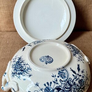 Puede incluir: Bol para servir de porcelana blanca con tapa, con un dise&ntilde;o floral azul. El bol tiene asas y un borde decorativo. La tapa es blanca lisa. El bol est&aacute; marcado con "Rocaille Terre de Fer, Salins".