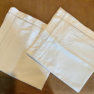 May include: Two white pillowcases with embroidered details. Each pillowcase features an embroidered monogram of the letters "SP" within a decorative design. The edges are finished with a stitched border and small decorative dots.