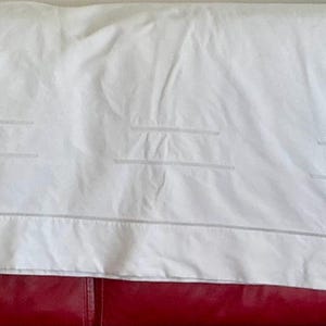 May include: A rectangular white fabric runner or tablecloth featuring a clean, minimalist design with subtle embroidered line details. The fabric has a smooth texture and is finished with a simple stitched border that frames the entire piece.