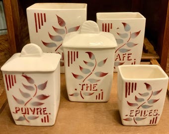 May include: Set of five white ceramic canisters with red and blue leaf designs. The canisters are labeled "The", "Cafe", "Epices", "Puyvre", and one is unlabeled.
