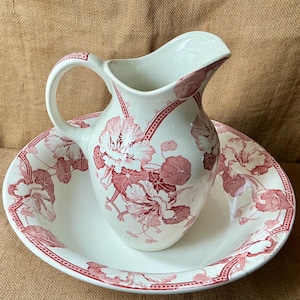 May include: Vintage white ceramic pitcher and basin set, decorated with a red floral pattern. The pitcher has a handle and spout, and the basin is circular. The set is a classic design.