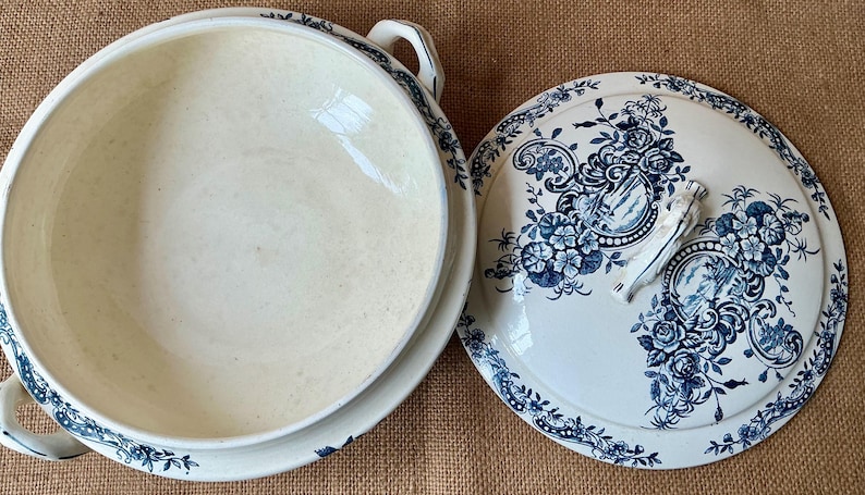 Puede incluir: Cuenco de cer&aacute;mica color crema con tapa a juego. La tapa y el borde del cuenco est&aacute;n decorados con un estampado floral azul. El cuenco tiene dos asas y la tapa tiene un asa.