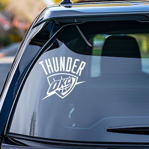 May include: White vinyl decal of the Oklahoma City Thunder logo with the word "THUNDER" above it. The logo features a basketball inside a shield with the letters "OKC" on it.