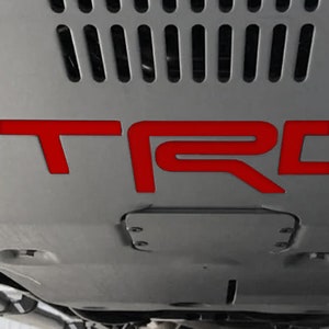 May include: A close-up of a gray undercarriage of a vehicle with a red "TRD" logo.