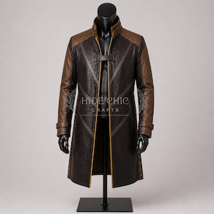 May include: A long, brown leather coat with contrasting brown and tan shoulder and sleeve panels. The coat features a high collar, a front closure, and decorative stitching. The brand name "HIDE CHIC CRAFTS" is visible on the front.