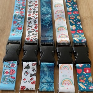 May include: Five colourful patterned lanyards with black plastic clips and silver swivel hooks. The lanyards feature a variety of designs, including medical symbols, rainbows, and abstract patterns.