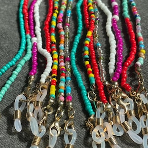 May include: A collection of colourful beaded eyeglass chains with gold clasps and clear silicone loops. The chains are made with small, round beads in various colours, including turquoise, red, white, pink, and yellow.