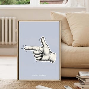 May include: A framed art print with a hand gesture pointing left, index finger extended and thumb up. The artwork is monochrome on a light blue background. The text "It's Not Working" is at the bottom of the print.