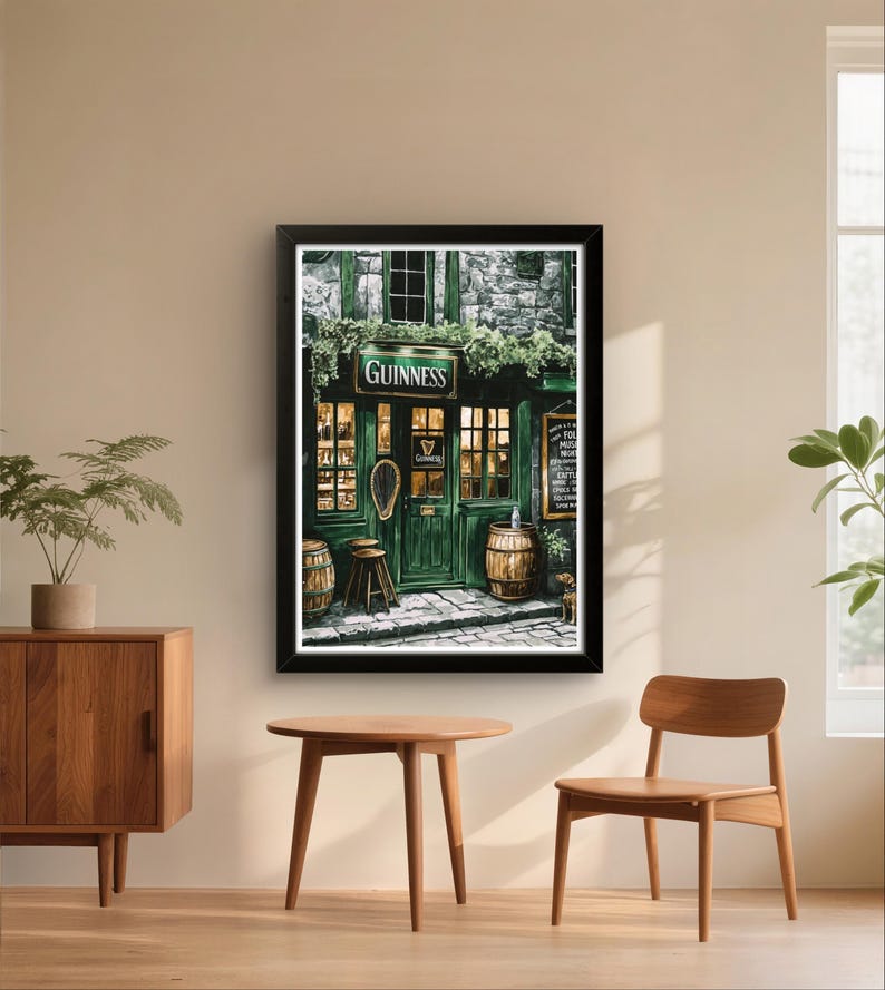 a framed painting of a pub with a green exterior and a sign that reads "GUINNESS". The painting is hanging on a wall, and there are two wooden chairs and a small table in front of it.