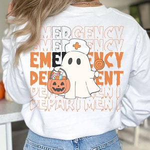 May include: A white long-sleeve sweatshirt featuring a graphic of a ghost dressed as a nurse holding a pumpkin candy bucket and a lollipop. The text EMERGENCY DEPARTMENT is repeated in the background in orange and black with a dripping font.