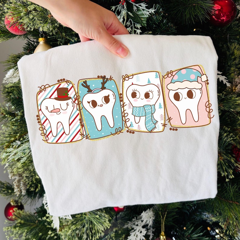May include: White sweatshirt featuring four cartoon teeth in festive frames. Each tooth is decorated with holiday-themed accessories like a hat, antlers, scarf, and a winter hat. The frames have colorful backgrounds and decorative borders.