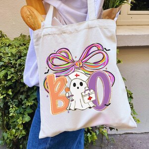 Pu&ograve; includere: Borsa tote in tela color crema con un design colorato "BOO". Il design presenta un fantasma con cappello da infermiera, una siringa e una borsa medica. Un grande fiocco multicolore e pipistrelli completano il tema di Halloween.