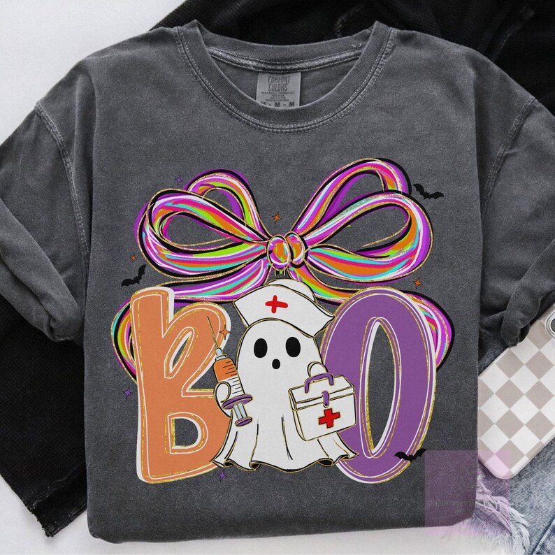 Pu&ograve; includere: Felpa grigio scuro con grafica "BOO" colorata. Il design presenta un fantasma con cappello da infermiera che tiene una siringa e una borsa medica, con un grande fiocco multicolore sopra. Piccoli pipistrelli sono sparsi.