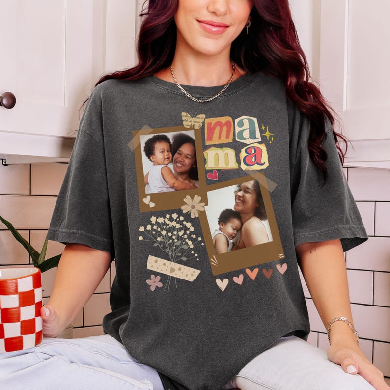 May include: Charcoal grey t-shirt with the word "mama" in colourful letters and two polaroid-style photos. The photos show a mother and child. The shirt also has decorative elements like hearts, flowers, and a butterfly.
