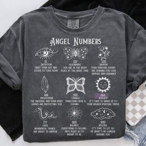 May include: Dark gray sweatshirt with white graphic of angel numbers and symbols. Text includes "Angel Numbers", "Intuition", "Alignment", "Support", "Protection", "Change", "Reflect", "Luck", "Balance", and "Release".