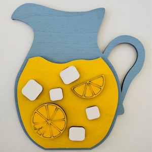 May include: A wooden pitcher painted blue with a yellow interior, filled with lemonade and ice cubes. The pitcher has a handle and is decorated with lemon slices.