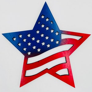 Puede incluir: Una estrella de madera recortada pintada en rojo, blanco y azul, que se asemeja a la bandera estadounidense. La estrella está recortada en forma de bandera, con el campo azul de estrellas en la parte superior y las rayas rojas y blancas en la parte inferior.