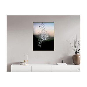 May include: A framed abstract art print with a central, dynamic composition of white, crystalline forms against a blurred backdrop of black, green, and a soft gradient of blue and peach. The artwork is displayed on a white cabinet.