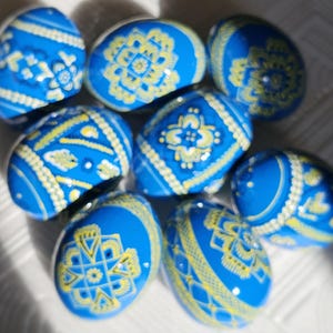 Op de afbeelding: Een verzameling blauwe paaseieren met ingewikkelde gele en witte bloempatronen. De eieren zijn in een cluster gerangschikt en tonen de gedetailleerde handgeschilderde ontwerpen. De eieren zijn helderblauw.