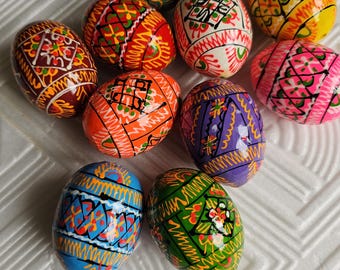 May include: A selection of brightly painted Easter eggs. Each egg displays detailed designs in various colours, including red, orange, yellow, green, blue, purple, and pink. The eggs are decorated with geometric and floral patterns.