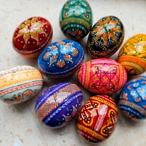 May include: A collection of ten hand-painted Easter eggs with intricate designs. The eggs are painted in various colors, including red, blue, green, yellow, and purple. Each egg features a unique pattern, including geometric shapes, floral motifs, and abstract designs.