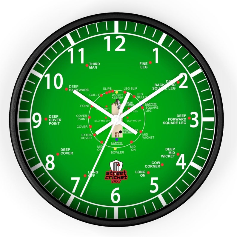 May include: A black and green clock with white numbers and hands. The clock face is a cricket field with the positions of fielders labeled. The clock face also includes the text "street cricket 24x7".