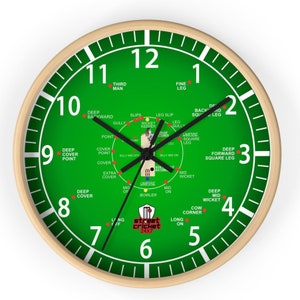 May include: A green and white clock with a cricket field layout. The clock face has numbers 1 through 12 and the positions of players on a cricket field are labeled around the clock face. The clock face also includes the text "street cricket 24x7".
