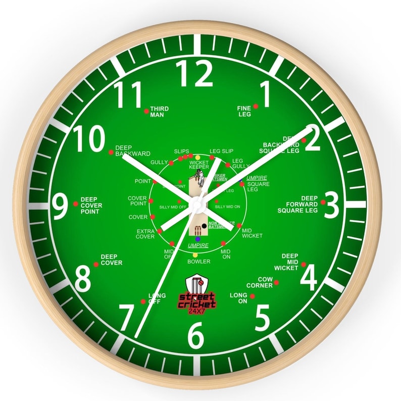 May include: A green and white clock with a cricket field design. The clock face shows the positions of fielders on a cricket pitch. The clock face also includes the text "street cricket 24x7".