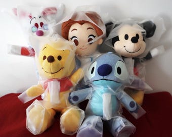 Könnte beinhalten: Fünf Plüschtiere, darunter Winnie Puuh, Stitch, Mickey Mouse, Belle und ein weißes Kaninchen, sind in durchsichtigem Plastik verpackt. Die Spielzeuge lächeln alle und haben ein freundliches Aussehen.