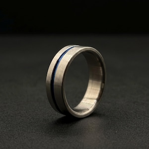 May include: A silver-colored ring with a brushed metal finish. A thin, vibrant blue line runs around the center of the ring. The ring is set against a dark background.