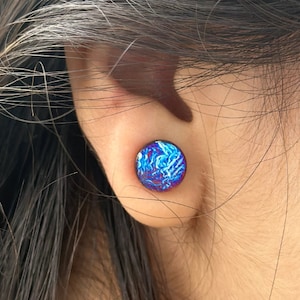 Puede incluir: Primer plano de la oreja de una persona con un dilatador de oreja azul y morado iridiscente. El dilatador tiene un patrón de remolino.
