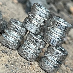 May include: A stack of five silver metal rings with a swirling pattern. The rings are stacked on top of each other, with the largest ring at the bottom and the smallest ring at the top.