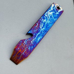 May include: A striking bottle opener with a distinctive design. The opener showcases a blue and white pattern, reminiscent of lightning, blending into orange and purple tones. It has a hole at the top for hanging, with a length of approximately 10 cm.