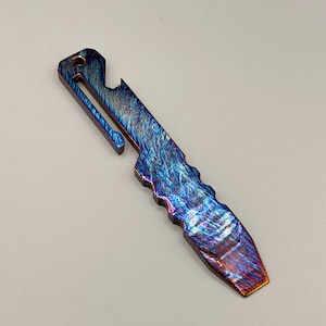 May include: A multi-tool with a vibrant, iridescent finish in shades of blue, purple, and orange. The tool features a bottle opener, a pocket clip, and a textured handle for grip. The overall design is sleek and modern.
