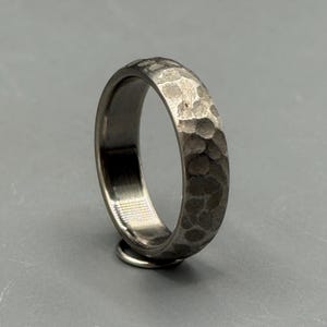 May include: A silver ring with a hammered texture. The ring features a textured band and a smooth, polished interior. The ring is displayed on a grey surface.