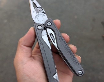Könnte beinhalten: Ein schwarzes Leatherman Charge Multitool mit Titan-Griffen. Das Werkzeug ist geöffnet, die Zange ist ausgefahren. Das Werkzeug verfügt über eine Vielzahl weiterer Werkzeuge, darunter ein Messer, eine Säge und einen Schraubendreher.