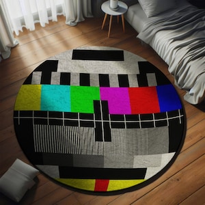May include: A round rug with a black and white television test pattern design. The pattern includes colored bars in yellow, blue, green, pink, red, and blue.