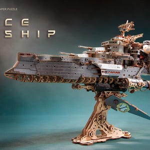 May include: A 3D wooden and paper puzzle of a space warship featuring intricate mechanical details, a long hull, and a central support stand. The text "howCat 3D WOODEN & PAPER PUZZLE" and "SPACE WARSHIP" is visible in the upper left corner of the image.
