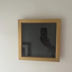 May include: A wooden picture frame with a black mount and a clear glass front. The frame is hanging on a white wall.