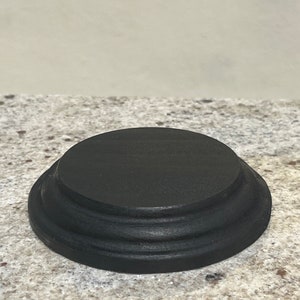 May include: A black wooden display stand with three tiers. The stand is round and has a smooth finish.