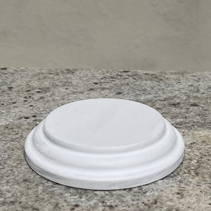 May include: A white, round, tiered pedestal with three layers. The pedestal is made of wood and has a smooth, painted finish.