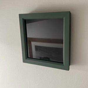May include: A dark green picture frame with a black mount and a reflection of a wooden beam in the glass.