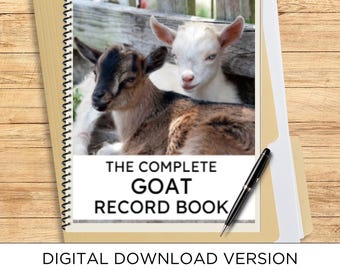 May include: A spiral-bound record book with a cover featuring a photograph of two young goats, one brown and black and one white, with the text THE COMPLETE GOAT RECORD BOOK printed below. A black ballpoint pen rests on the cover.