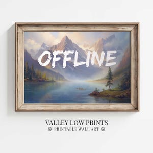 Puede incluir: Una impresión enmarcada de una escena de lago de montaña con la palabra "OFFLINE" escrita en blanco sobre la imagen. La impresión está en un marco de madera con un acabado marrón claro. La impresión se titula "Valley Low Prints - Printable Wall Art".