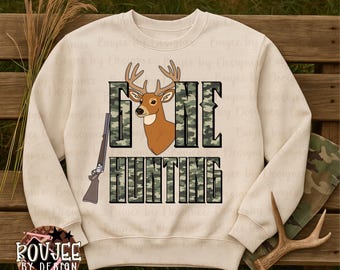 Puede incluir: Sudadera de color crema con un gráfico de ciervo y las palabras "GONE HUNTING" en estampado de camuflaje. Un rifle está representado en el lado izquierdo del diseño. La sudadera tiene cuello redondo y mangas largas.