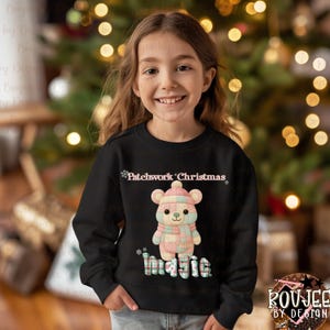 May include: A black sweatshirt with a bear design wearing a hat and scarf, with the words "Patchwork Christmas" and "magic". The bear is in pastel colours. The sweatshirt is worn by a young person, in front of a Christmas tree.