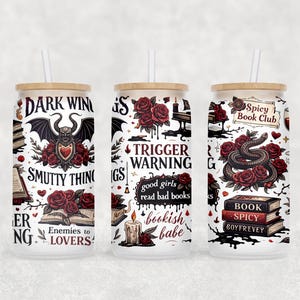 Op de afbeelding: Drie glazen bekers met bamboe deksels en witte rietjes. Elke beker heeft een uniek ontwerp met gotische en romantische elementen, waaronder rozen, een slang en tekst zoals "Dark Wings, Smutty Things" en "Spicy Book Club".