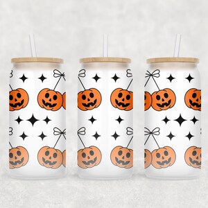 Op de afbeelding: Drie glazen bekers met een Halloween-thema. Elke beker heeft een herhalend patroon van oranje pompoenen, zwarte stervormen en een witte achtergrond. De bekers hebben houten deksels en doorzichtige rietjes.
